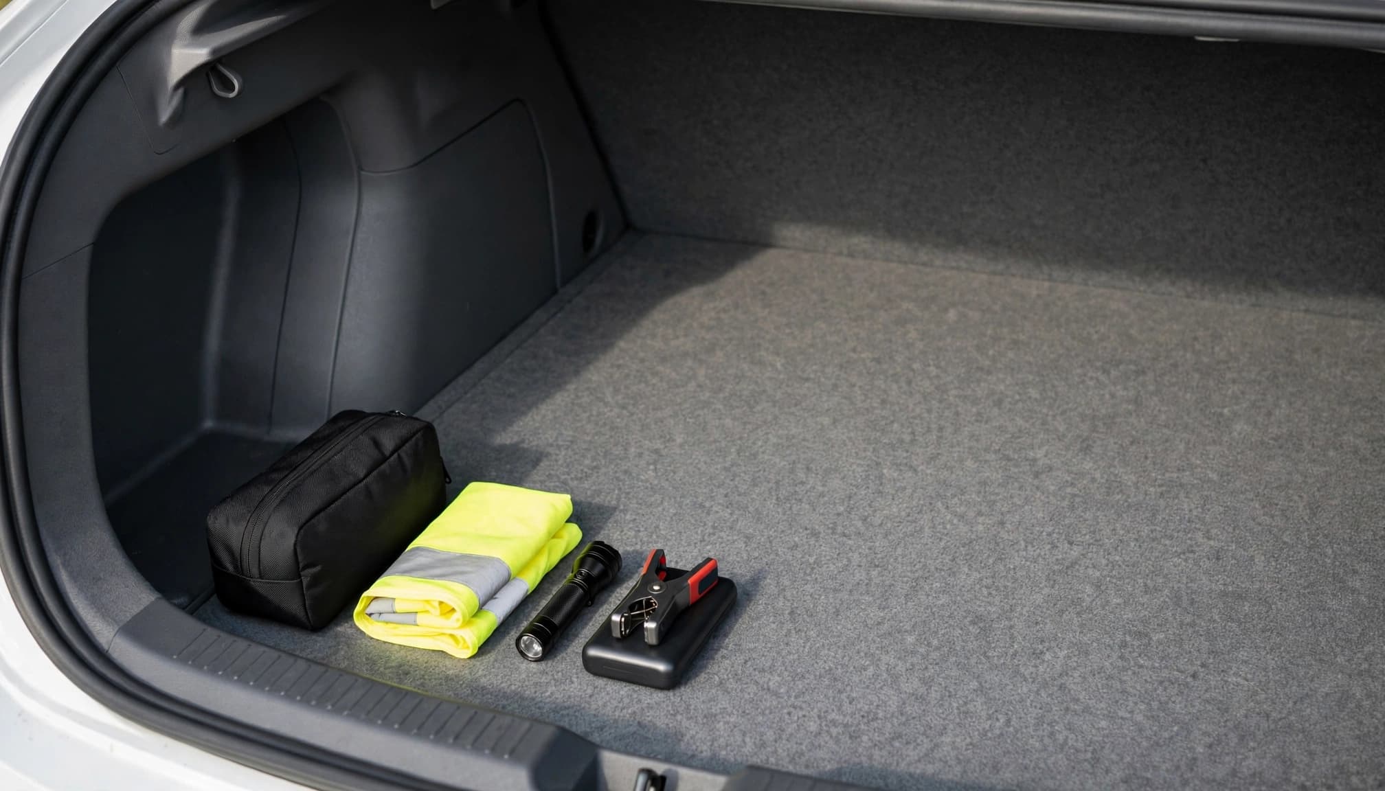 A small emergency kit and a few essentials sit in one corner of a mostly empty sedan trunk.